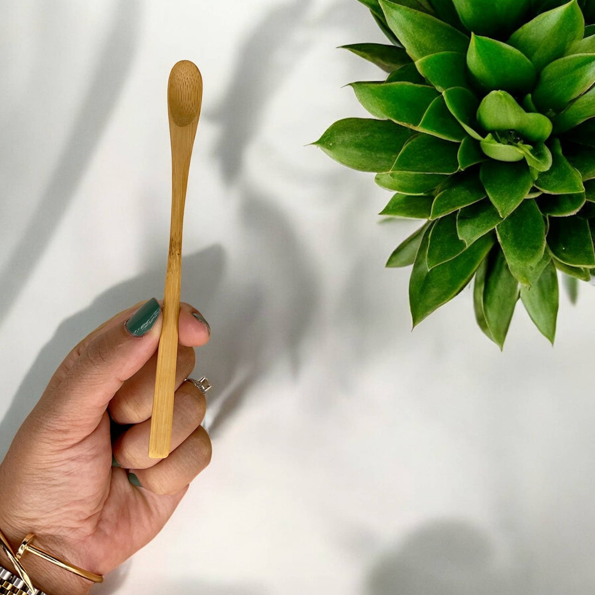 Light bamboo long stir spoon with rounded end, held in one hand
