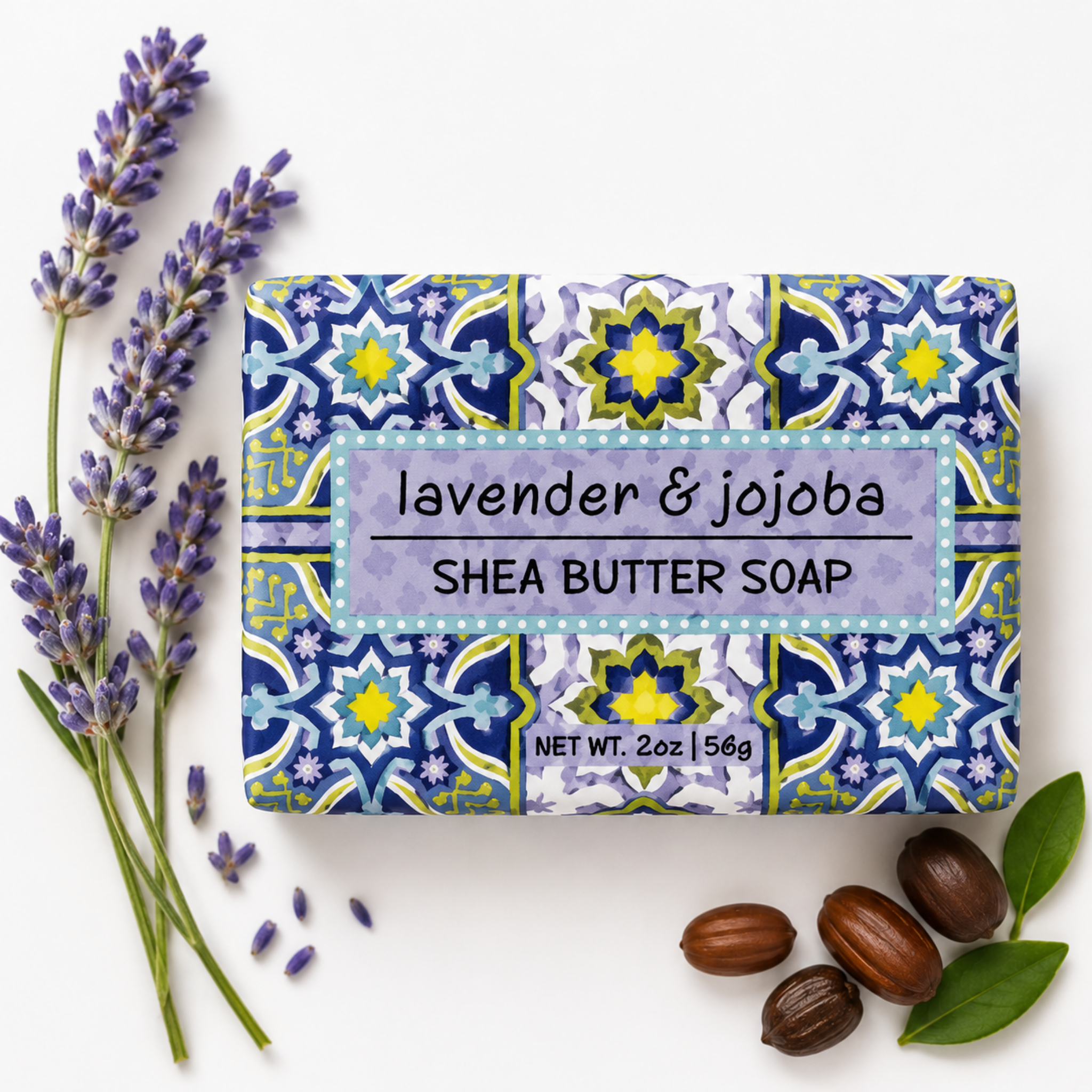 A rectangular bar of lavender & jojoba shea butter soap with a blue, yellow, and white geometric tile pattern, styled on a white background with lavender sprigs, jojoba seeds, and green leaves.
