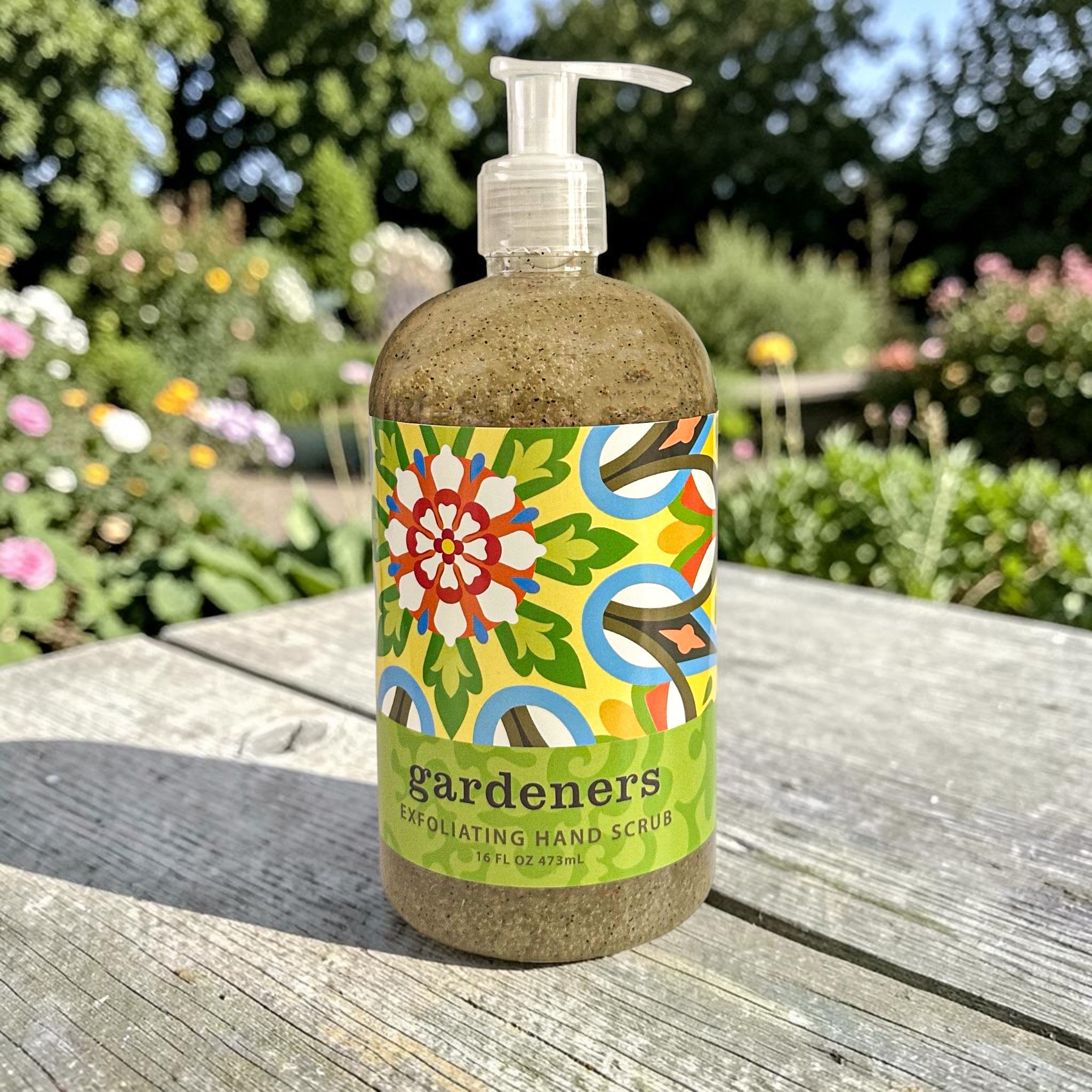 Bottle of 'Gardeners' exfoliating hand scrub with a colorful label on a wooden surface outdoors.