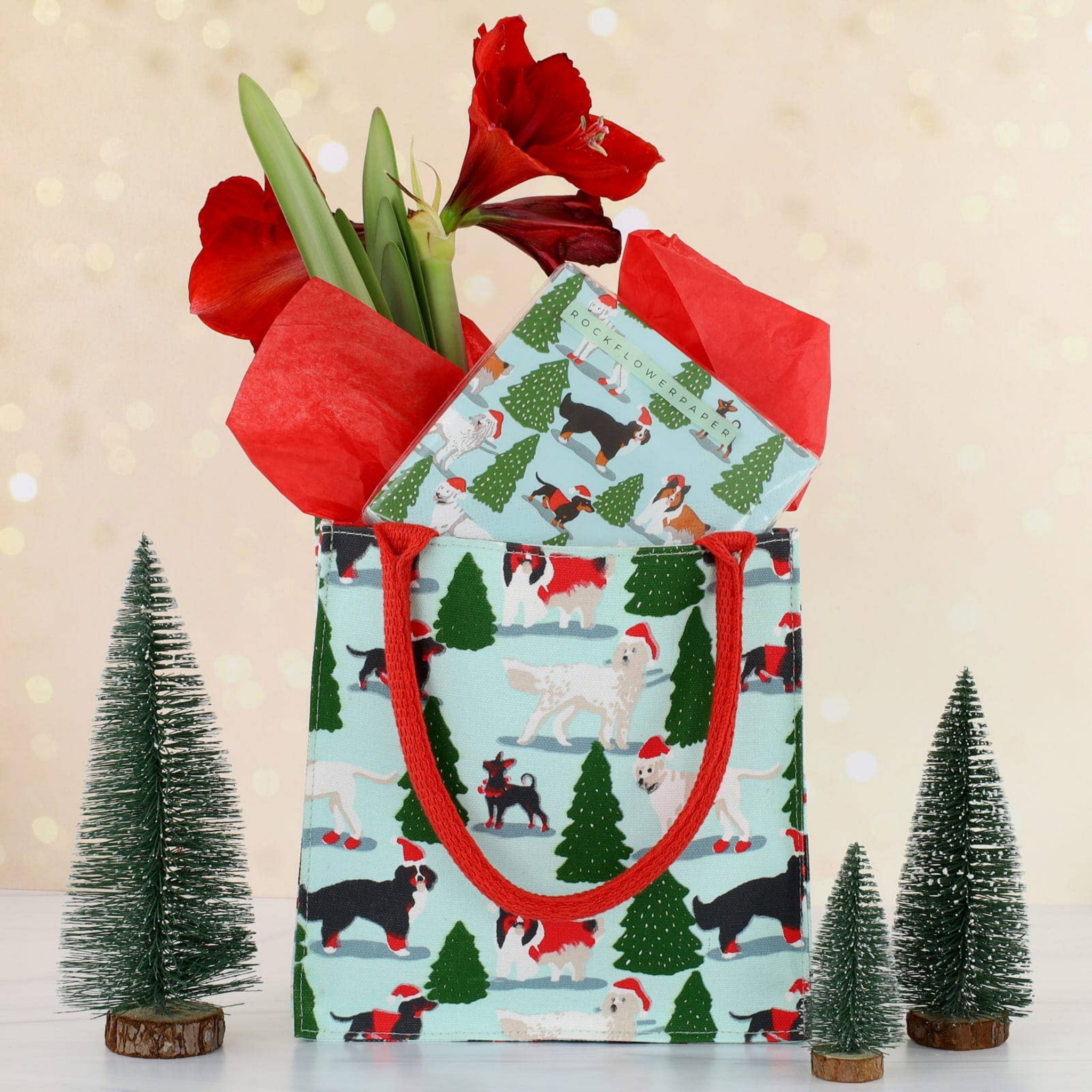 Gift bag with Christmas tree and dog pattern, filled with red tulips, on a festive background.