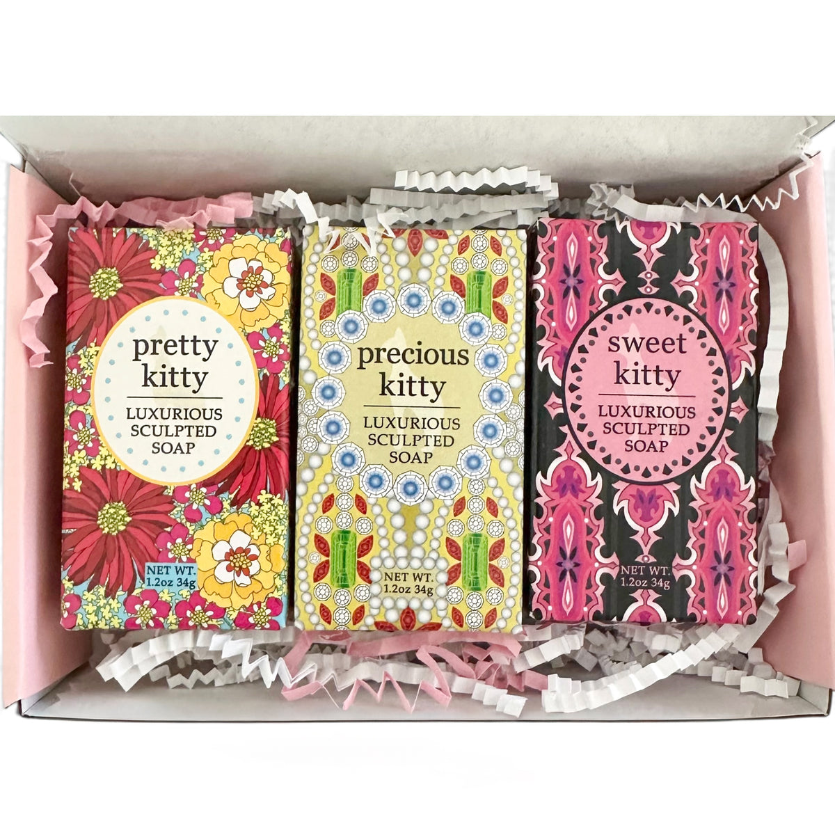 Three decorative soap bars in colorful patterned boxes arranged inside a pink gift box with white shredded paper. The soaps are labeled 'pretty kitty', 'precious kitty', and 'sweet kitty luxurious sculpted soap'.