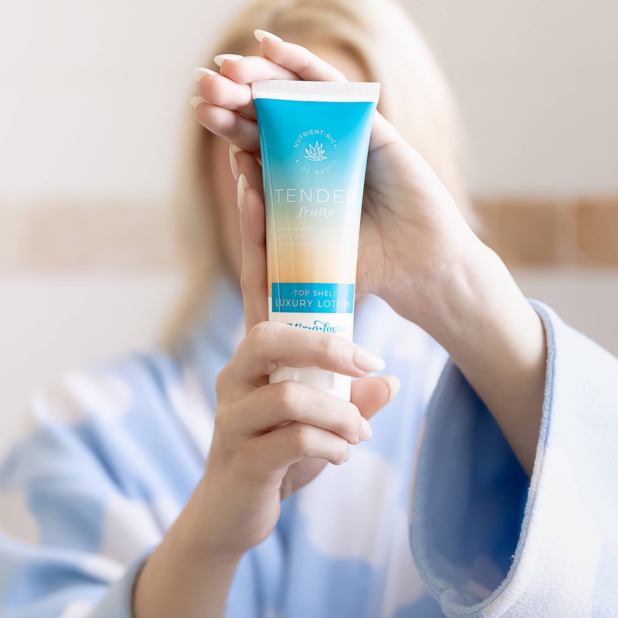 Person holding a tube of 'Tender' body lotion with a blurred background