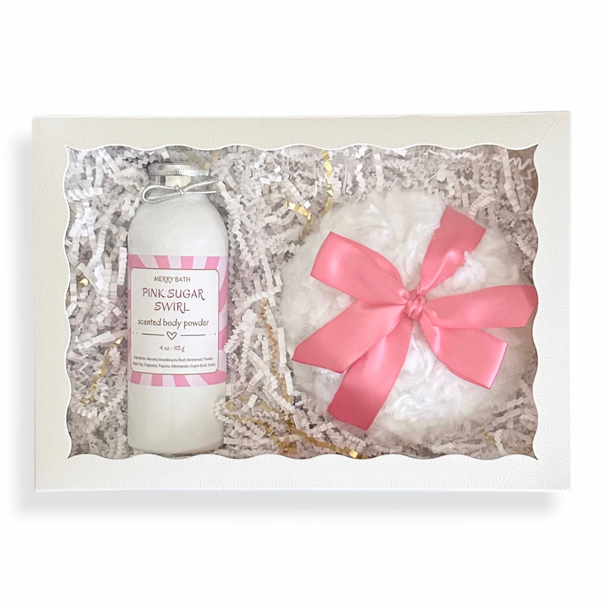A gift set containing a bottle of 'Pink Sugar Swirl' natural body powder and a fluffy white bath bomb wrapped in a pink ribbon, presented in a white box filled with white shredded paper.