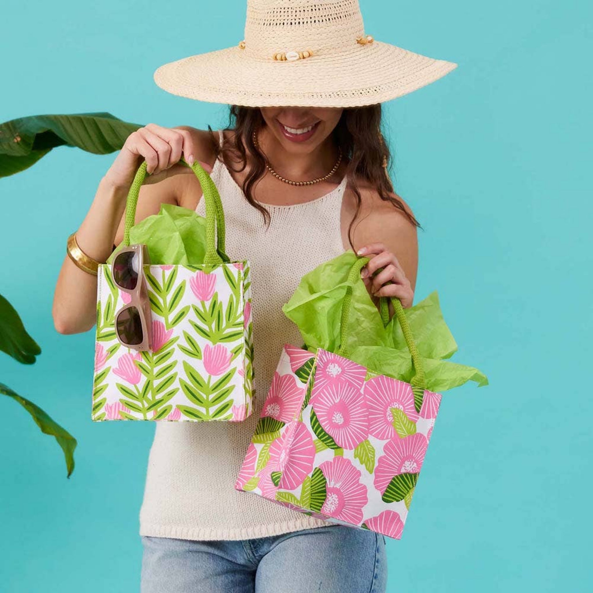 Reusable gift bag with pink and green leaf floral print, held by green handles