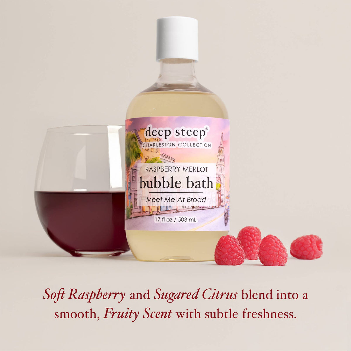 A bottle of deep steep Charleston Collection Raspberry Merlot bubble bath stands on a light beige background next to a glass of dark red liquid and four raspberries. Text below reads: 'Soft Raspberry and Sugared Citrus blend into a smooth, Fruity Scent with subtle freshness.