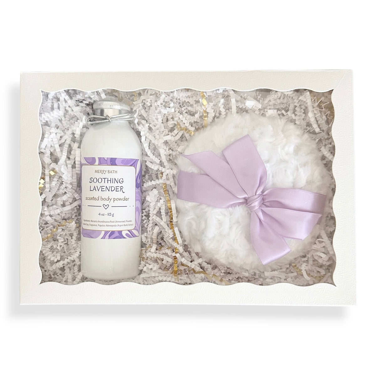 A gift set in a white box with shredded paper filler, containing a bottle of Mended Skin Soothing Lavender infused body powder and a white bath bomb with a light purple ribbon bow.