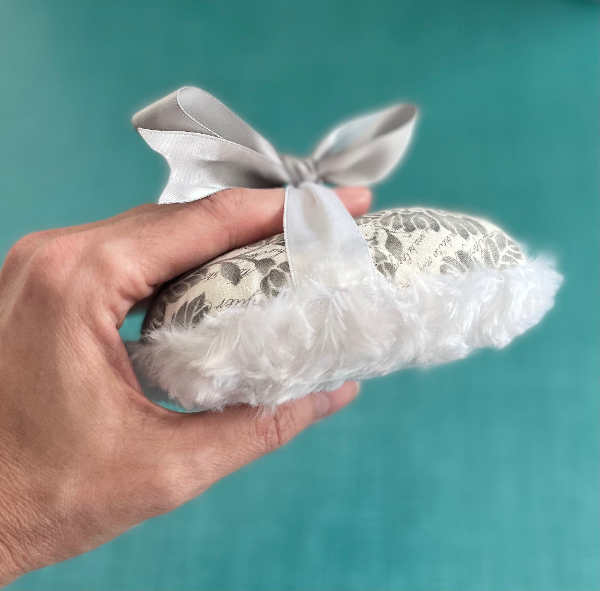 Gray-and-white floral powder puff in hand, satin bow with fluffy white edge
