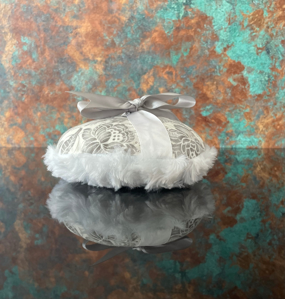 Large circular powder puff with gray floral top, white fluffy trim, and pale satin bow