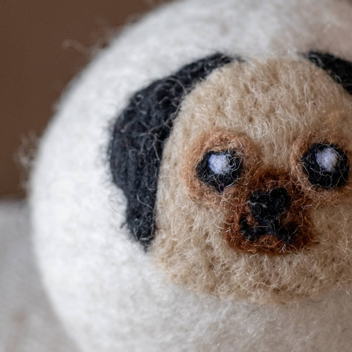 Close-up of natural wool dryer ball with dog-face embroidery in tan, black, and cream