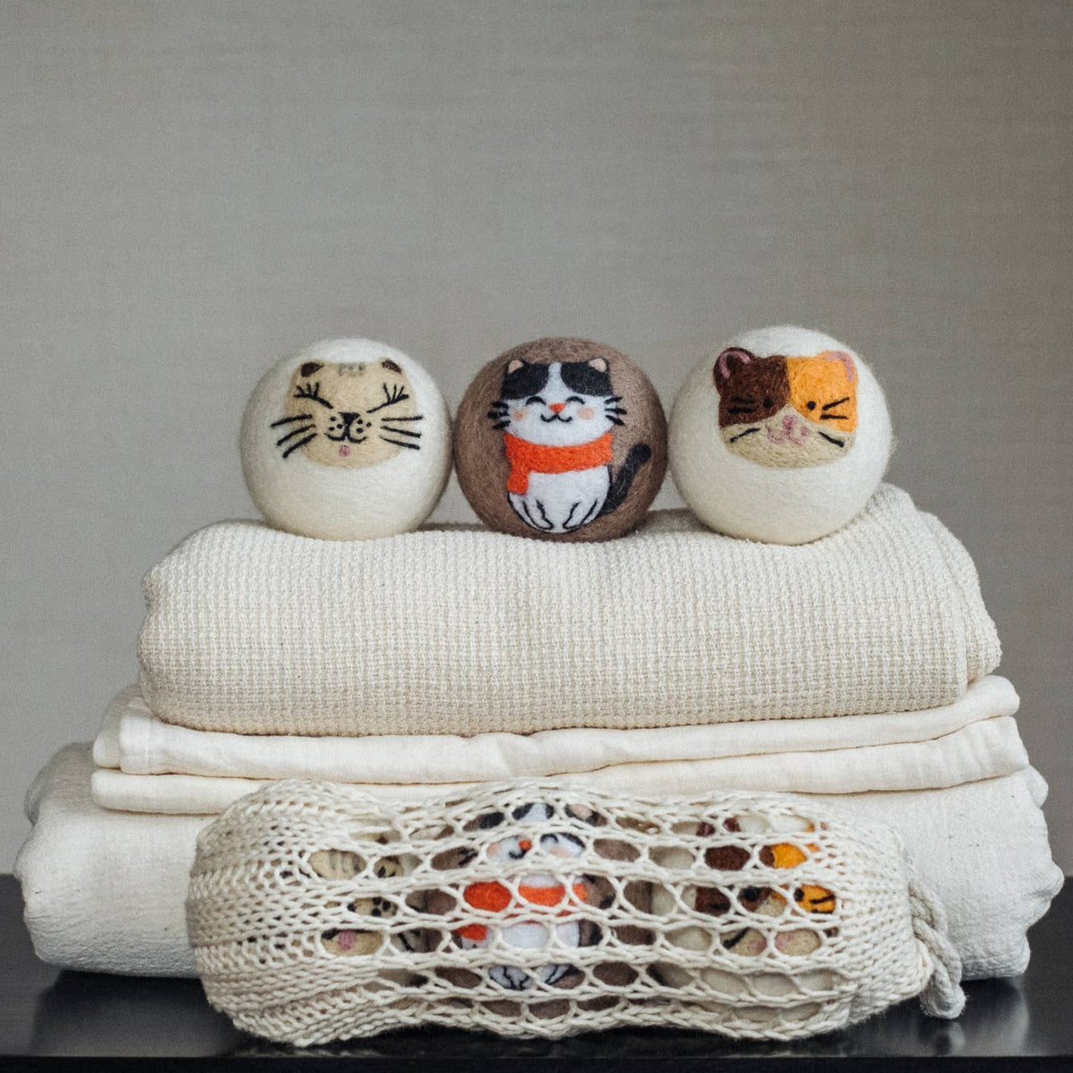 Natural wool dryer balls gift set of 3, three stacked cat-face dryer balls on linens