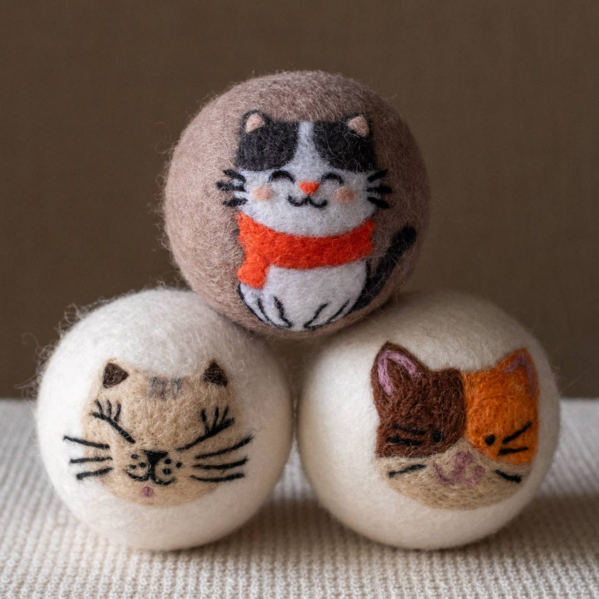 Natural wool dryer balls gift set of 3, three cat-face balls close-up on textured fabric