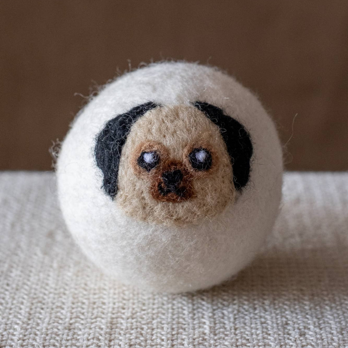 Natural wool dryer ball with stitched dog face, black ears and tan muzzle on white wool