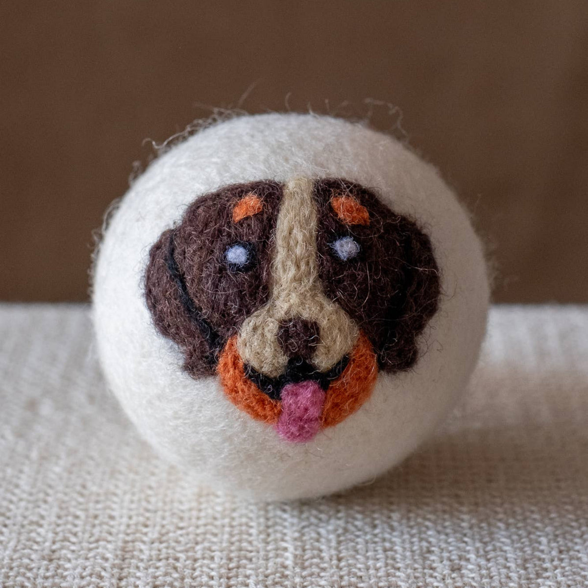 Natural wool dryer ball with stitched dog face, dark fur and orange-pink nose