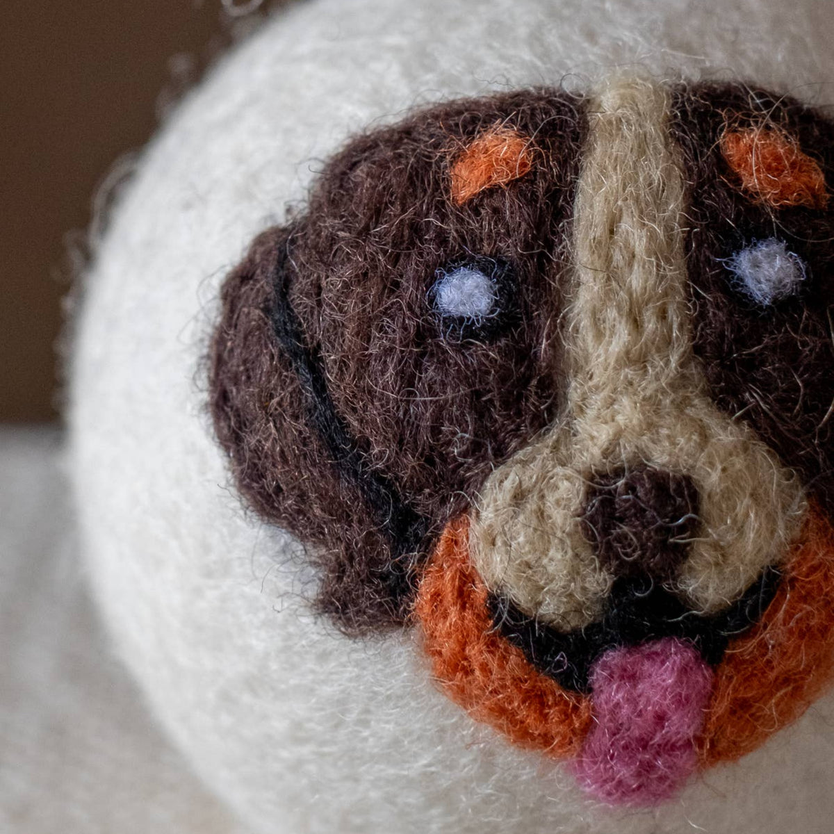 Close-up of natural wool dryer ball with dog-face embroidery and orange-pink muzzle