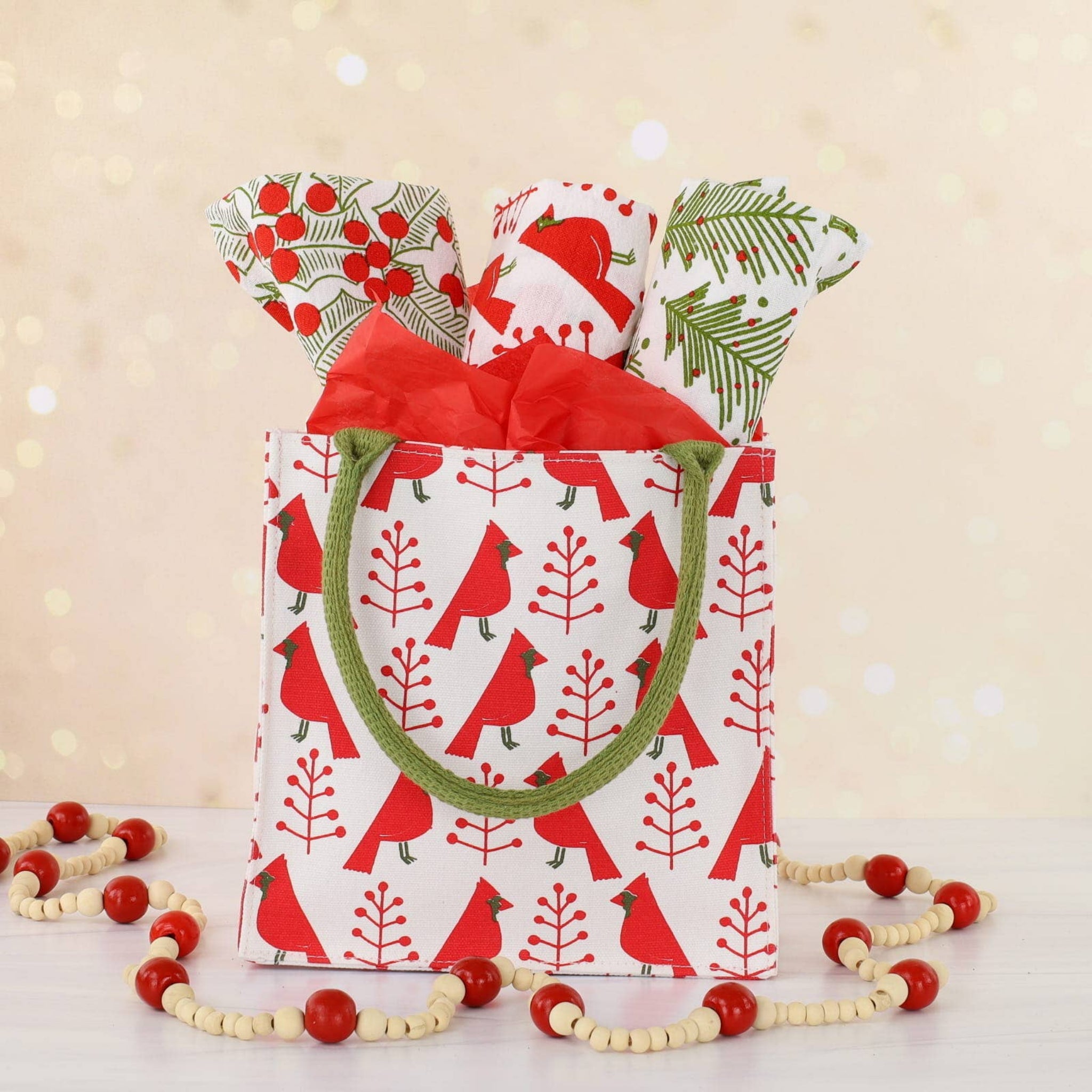 Decorative gift bag with red birds and greenery design, featuring a red ribbon and green handle on a beige background.