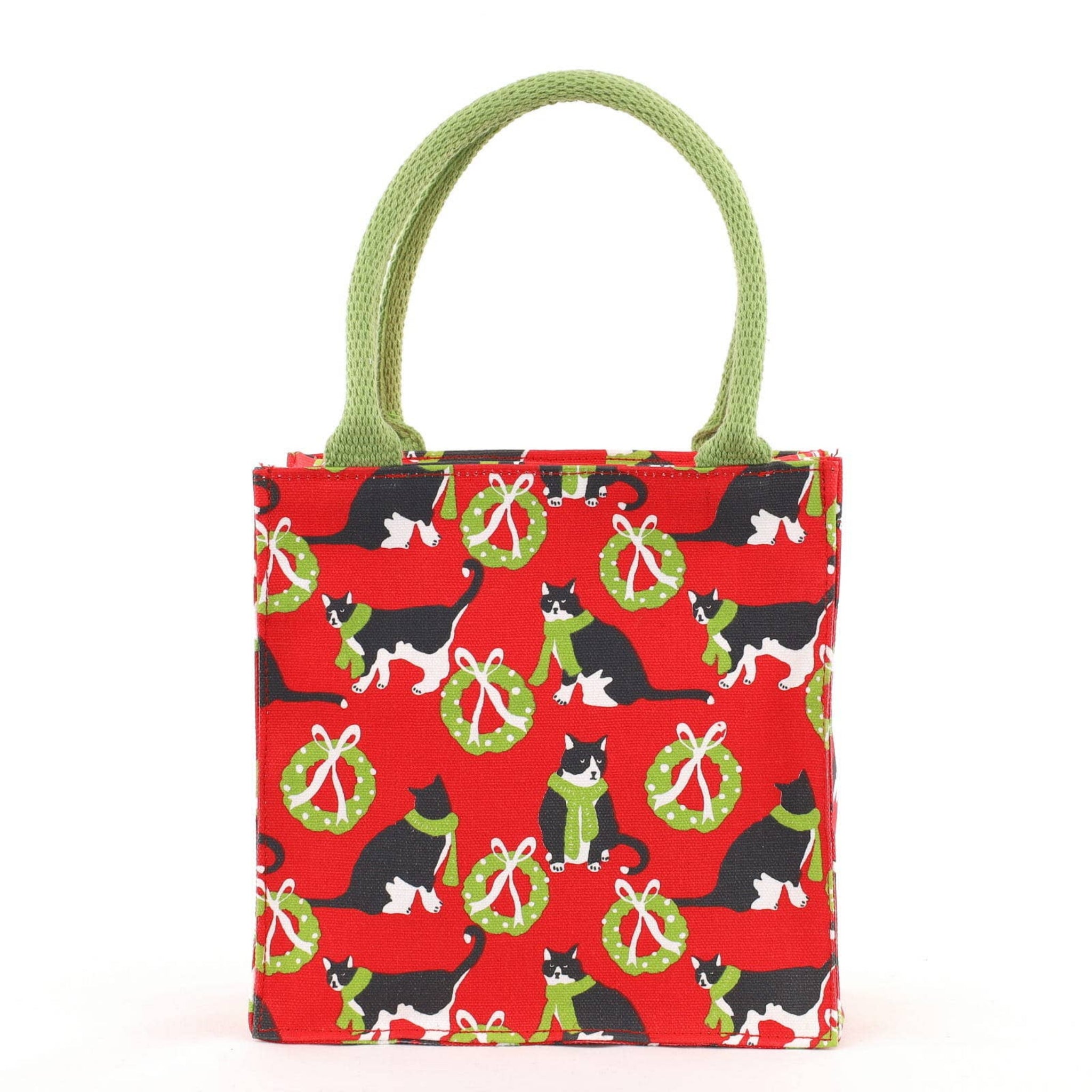 A small fabric tote bag with a red background printed with black and white cats, green wreaths, and light green handles, photographed on a clean white background.