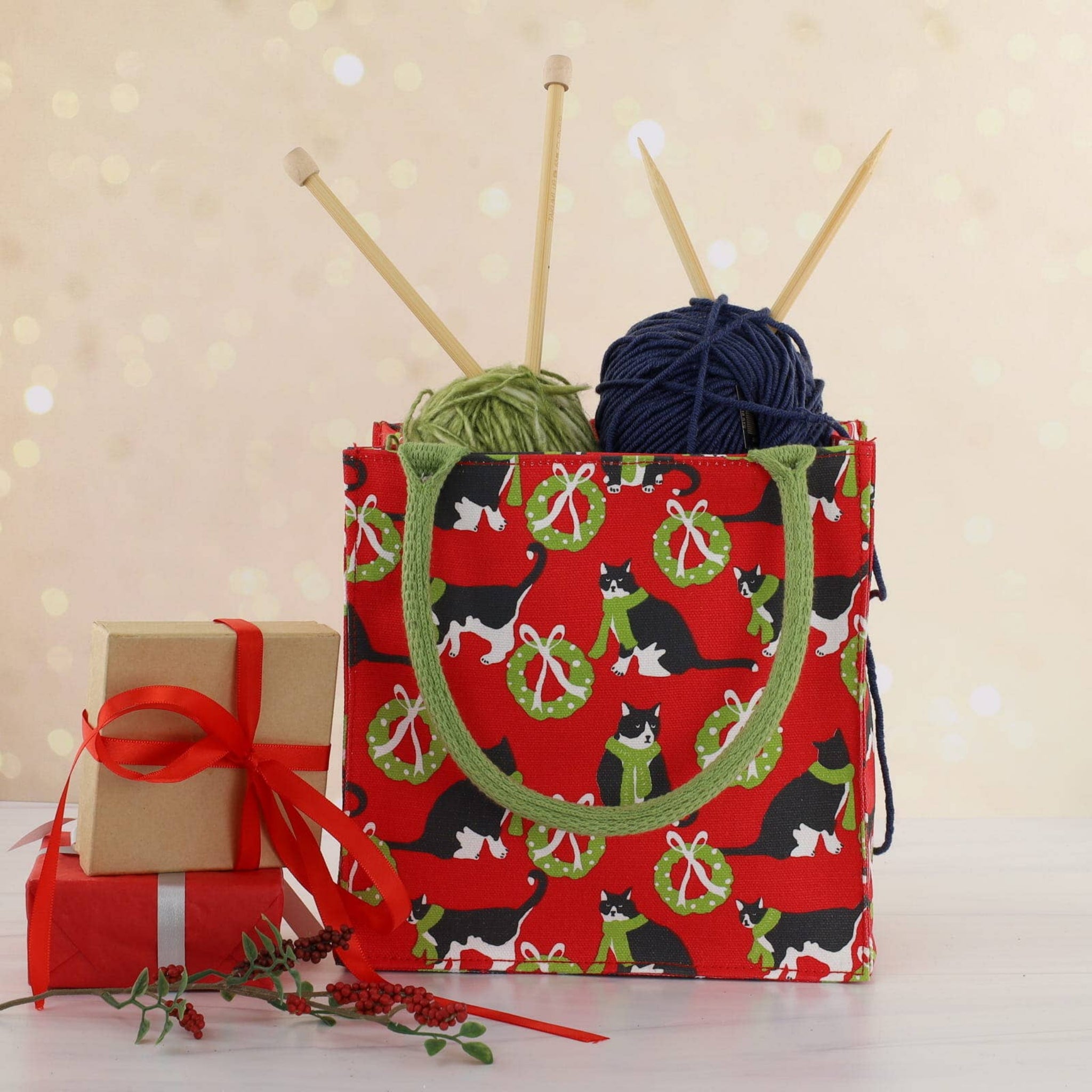 Red bag with cat pattern, yarn, and knitting needles on a light background