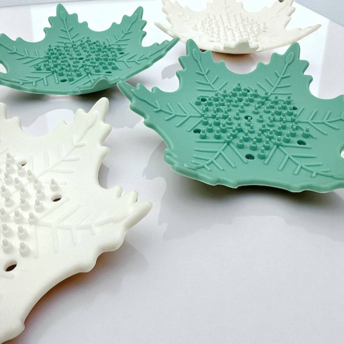 Two green leaf-shaped coasters on a white surface with seashells.
