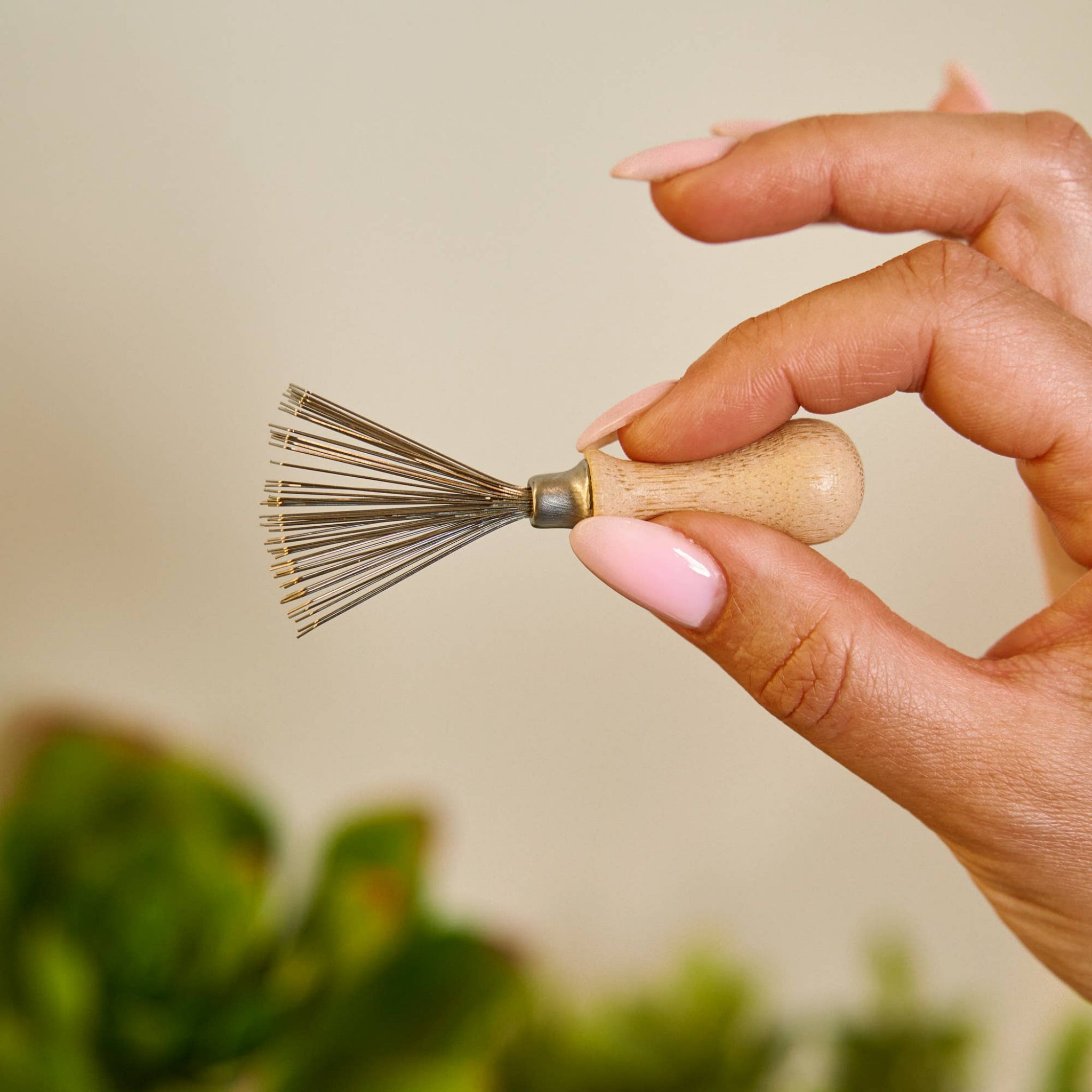 Hairbrush cleaning tool with wooden handle and metal pin bristles, held in hand