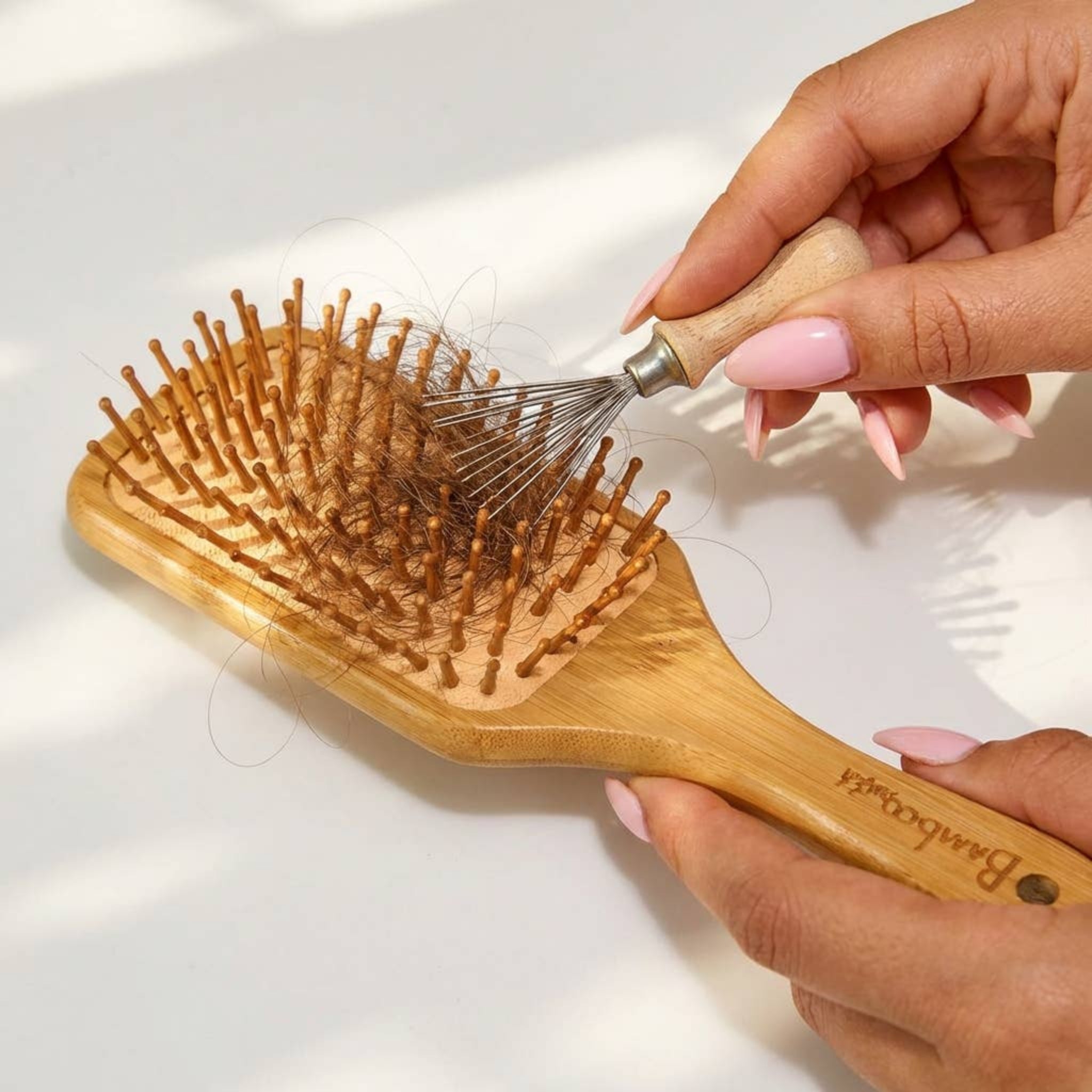 Hairbrush cleaning tool removing debris from a wooden hairbrush with metal pins