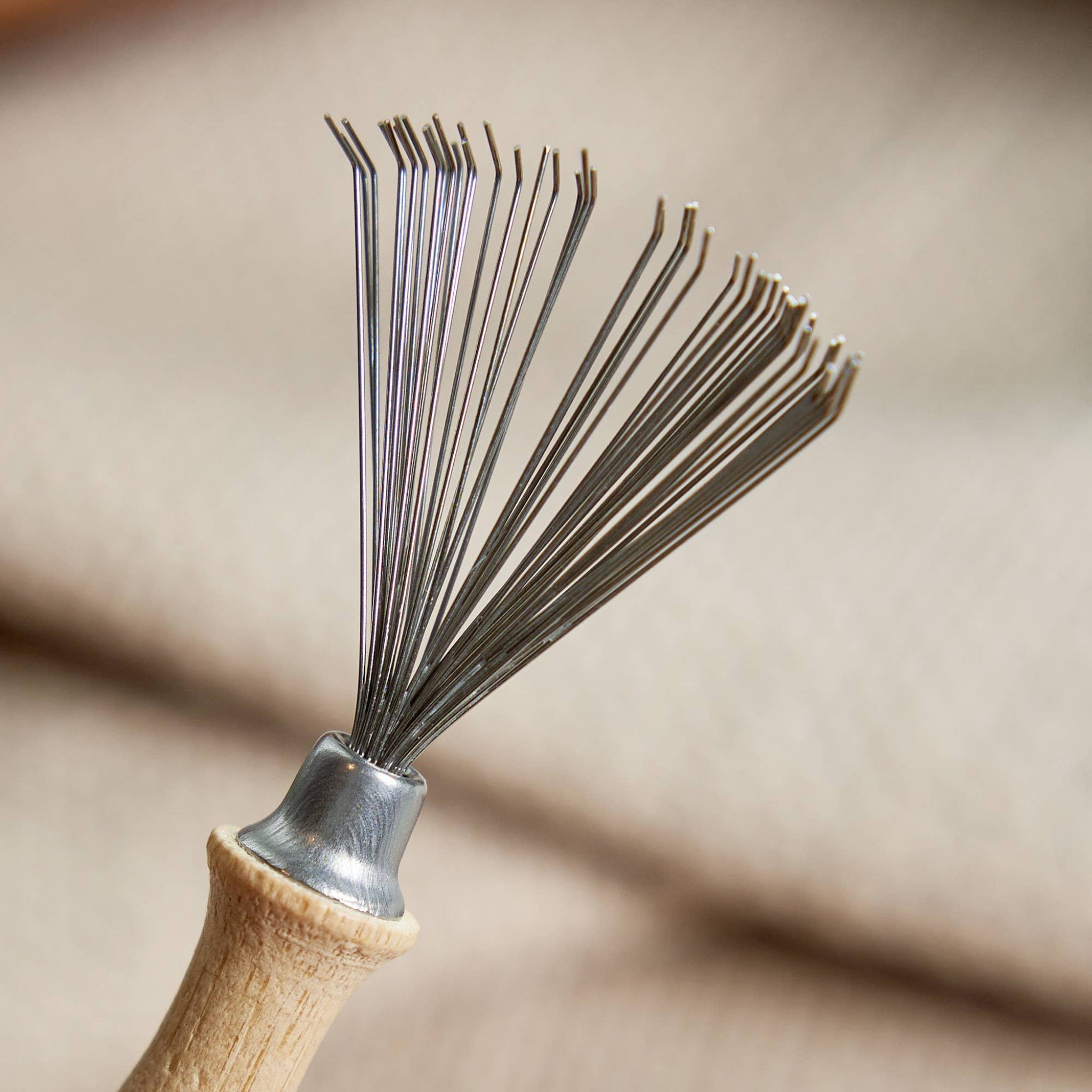 Hairbrush cleaning tool close-up: metal pin bristles on wooden handle