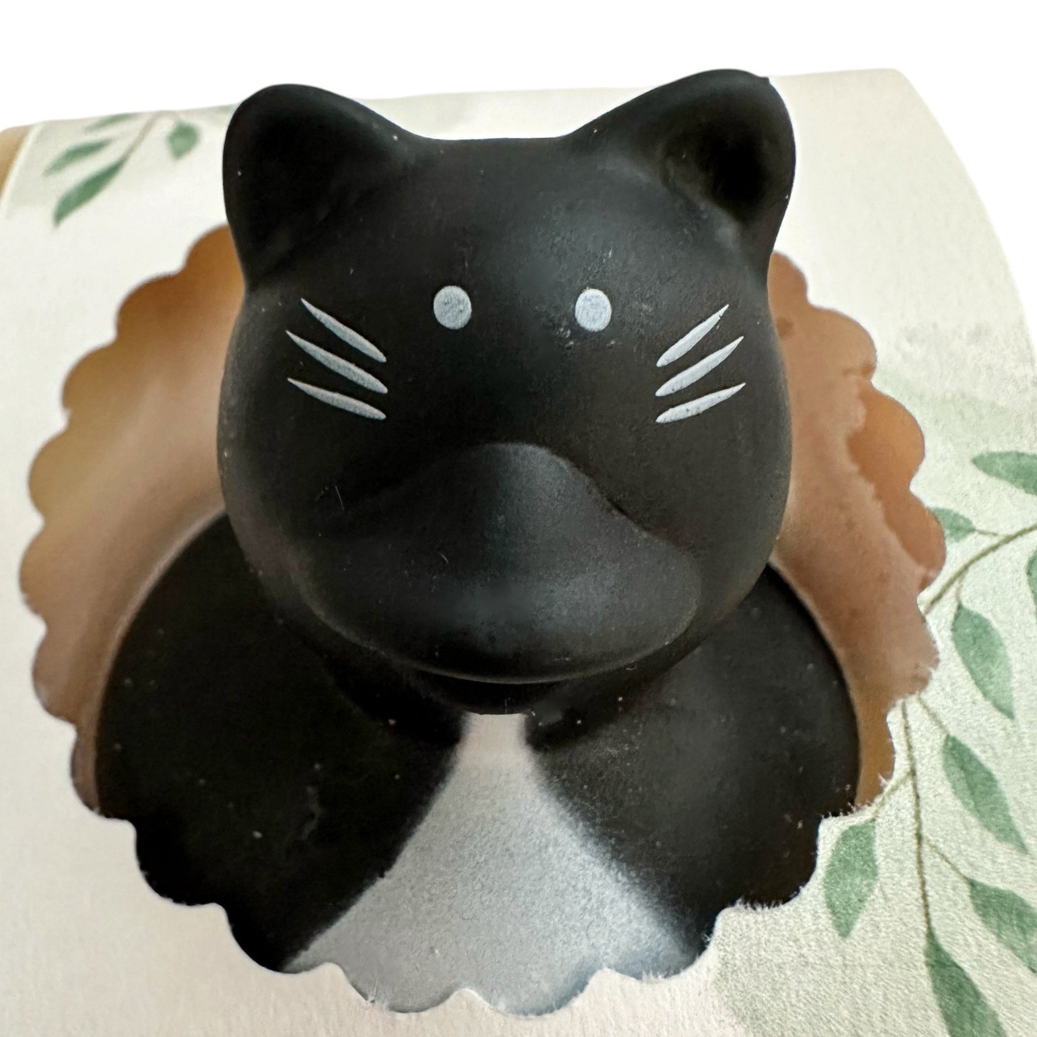Handmade soap bar shaped like a black cat with light eyes and whisker details.
