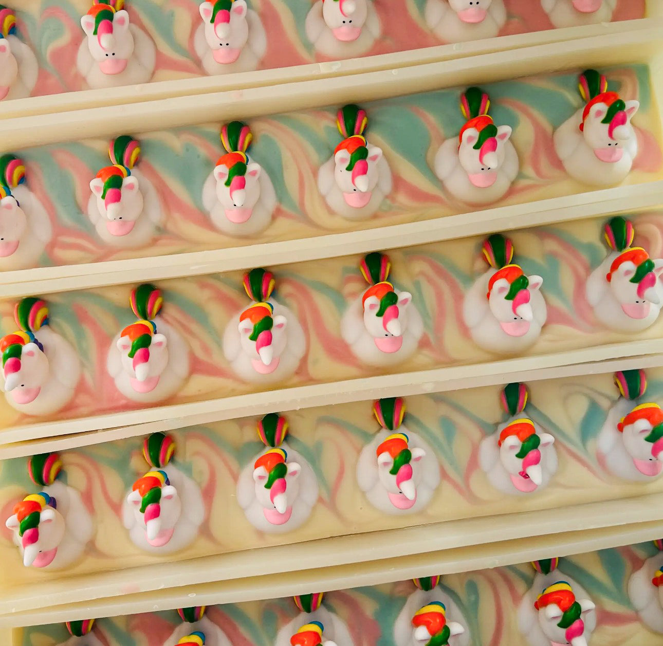 Pattern of pastel yellow handmade soap bars, each topped with a unicorn face decoration.