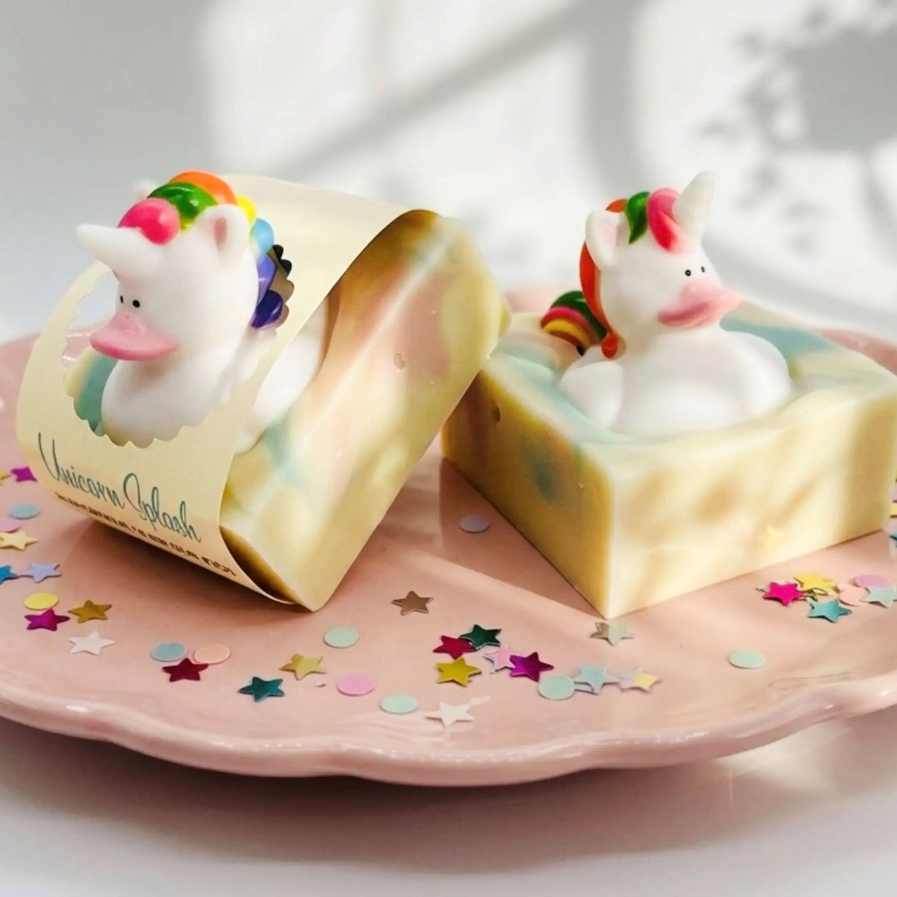 Pastel yellow handmade soap bar with unicorn face and multicolor mane, shown on a plate.