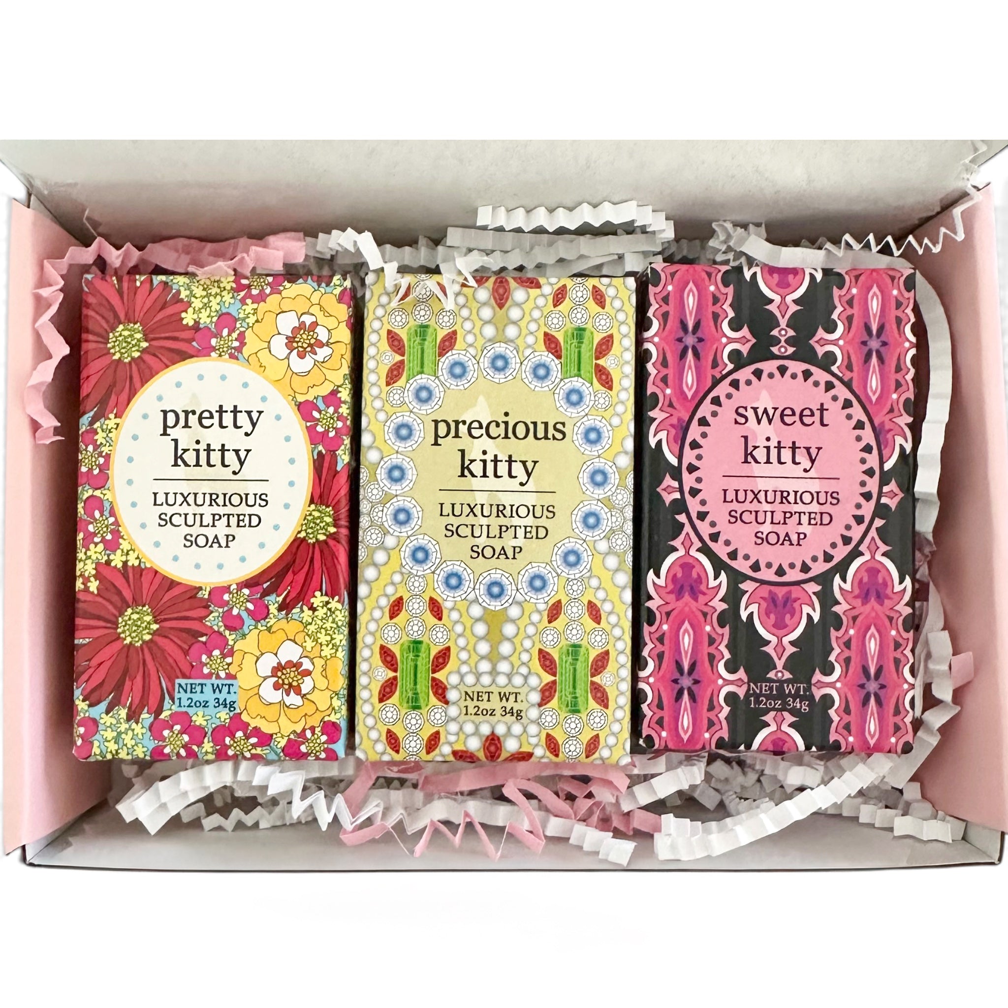 Three decorative soap bars in colorful patterned boxes arranged inside a pink gift box with white shredded paper. The soaps are labeled 'pretty kitty', 'precious kitty', and 'sweet kitty luxurious sculpted soap'.
