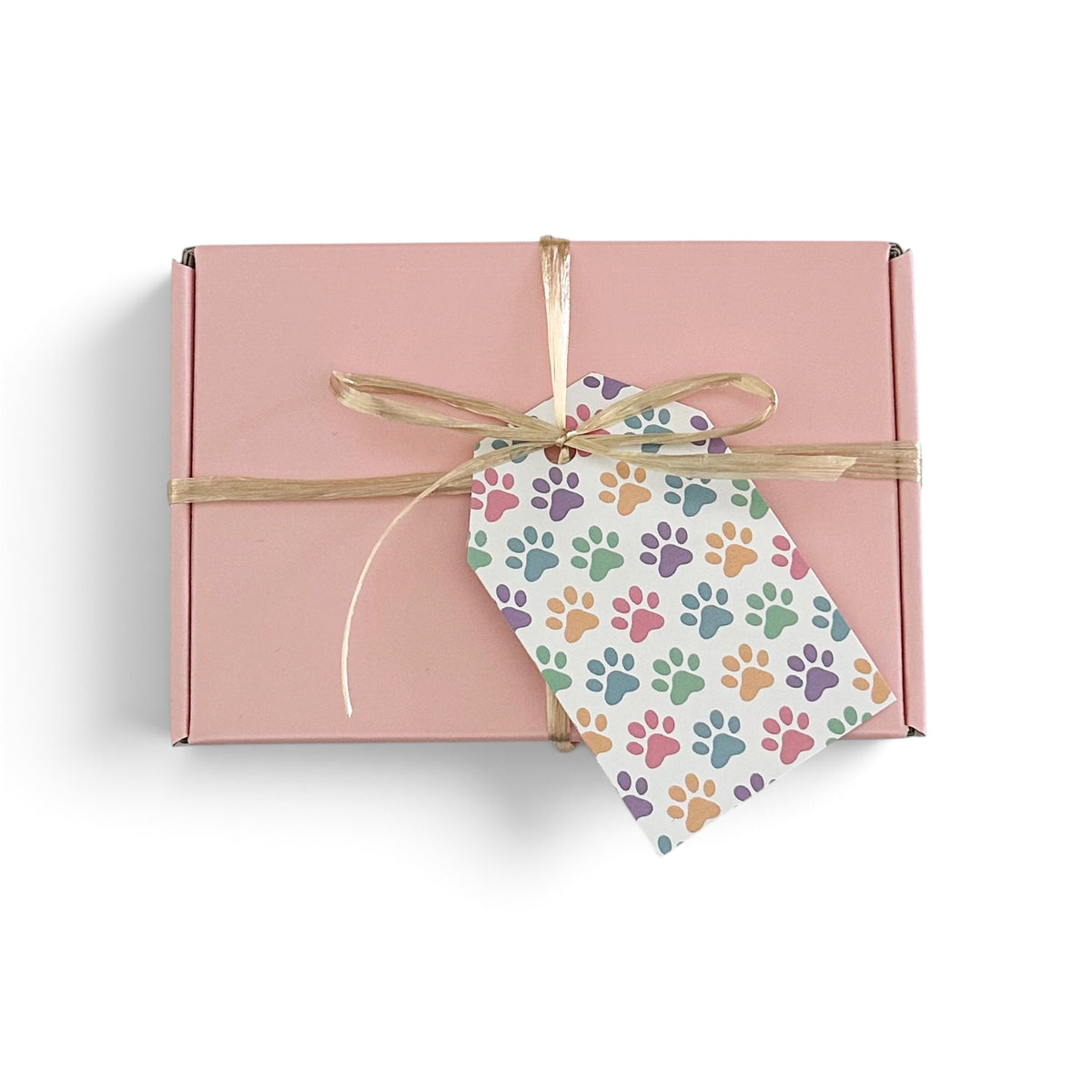 A pink rectangular gift box tied with a gold ribbon and a white paper tag printed with colorful paw prints, shown on a clean white background.