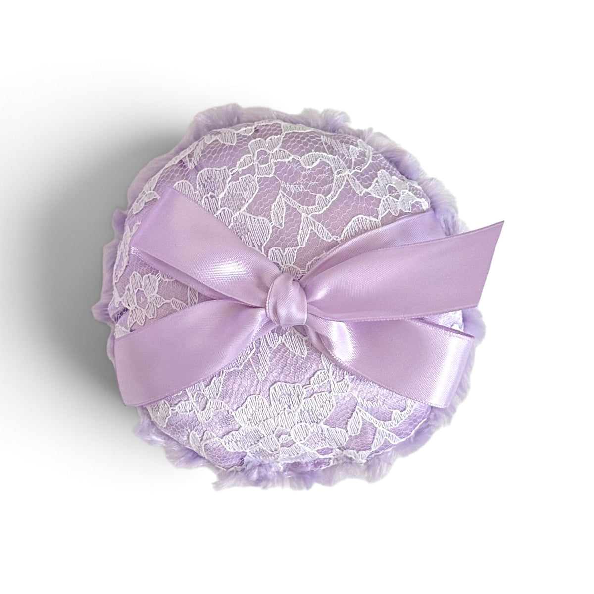 A round lavender and white lace pillow with a large satin bow, photographed on a white background with a soft shadow.