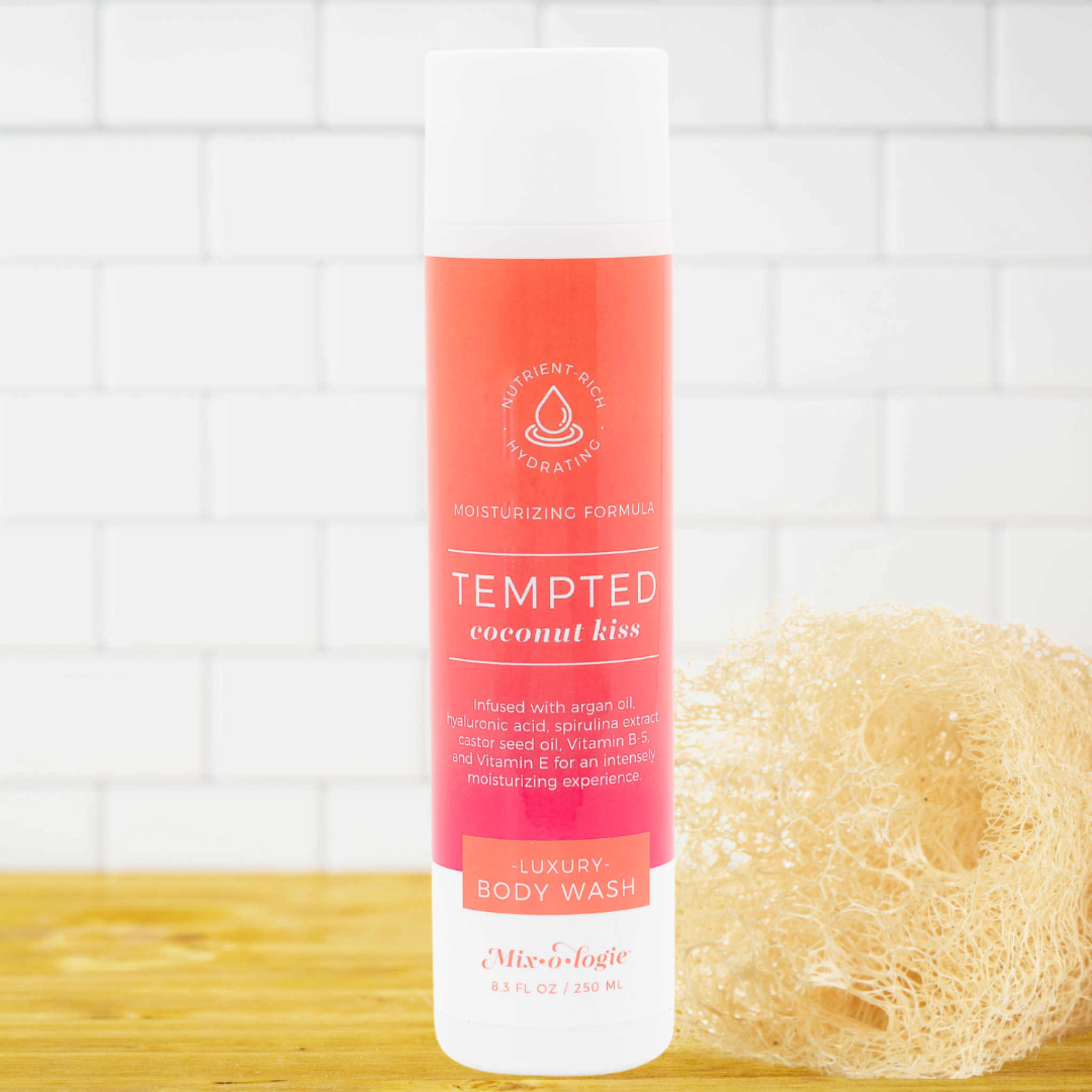 Body wash bottle labeled 'Tempted Coconut Kiss' with a loofah on a wooden surface and tiled wall background.