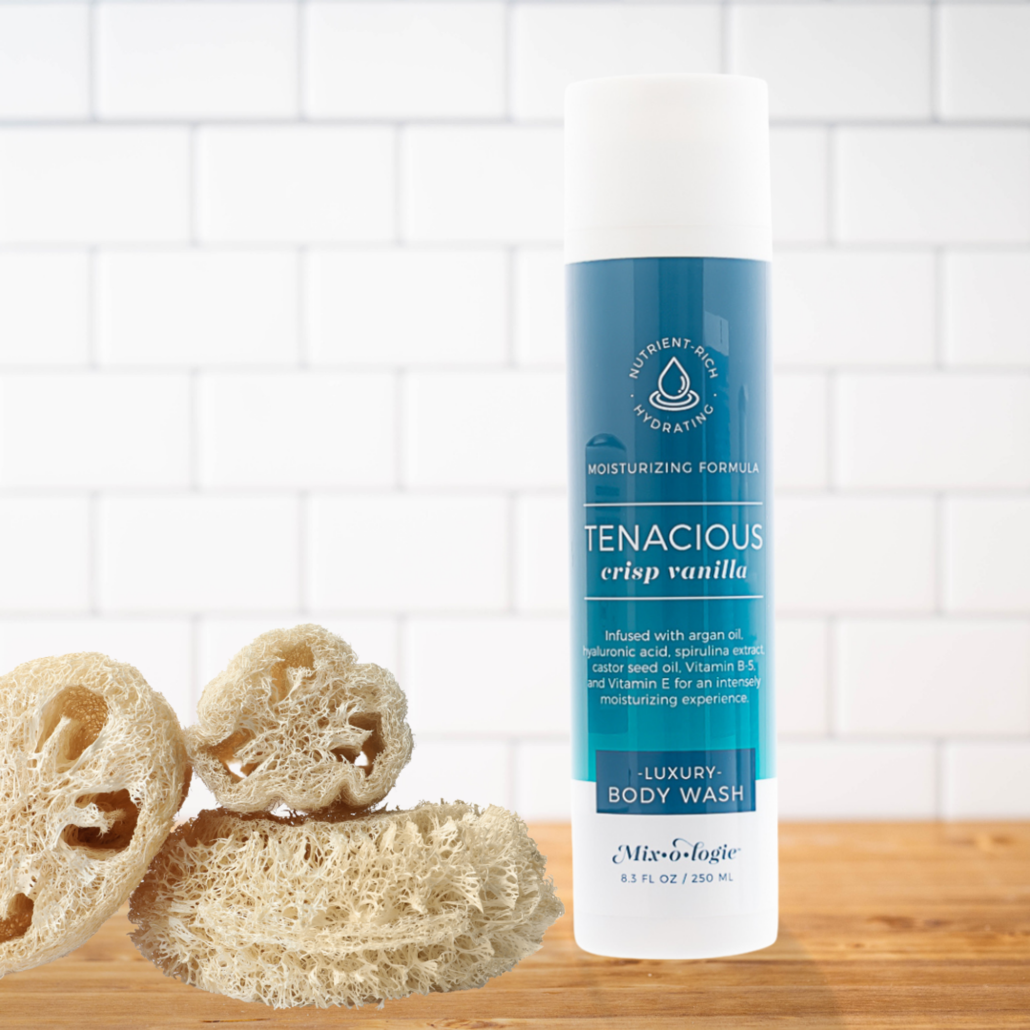 Body wash bottle labeled 'Tenacious' with natural sponges on a wooden surface and tiled wall background