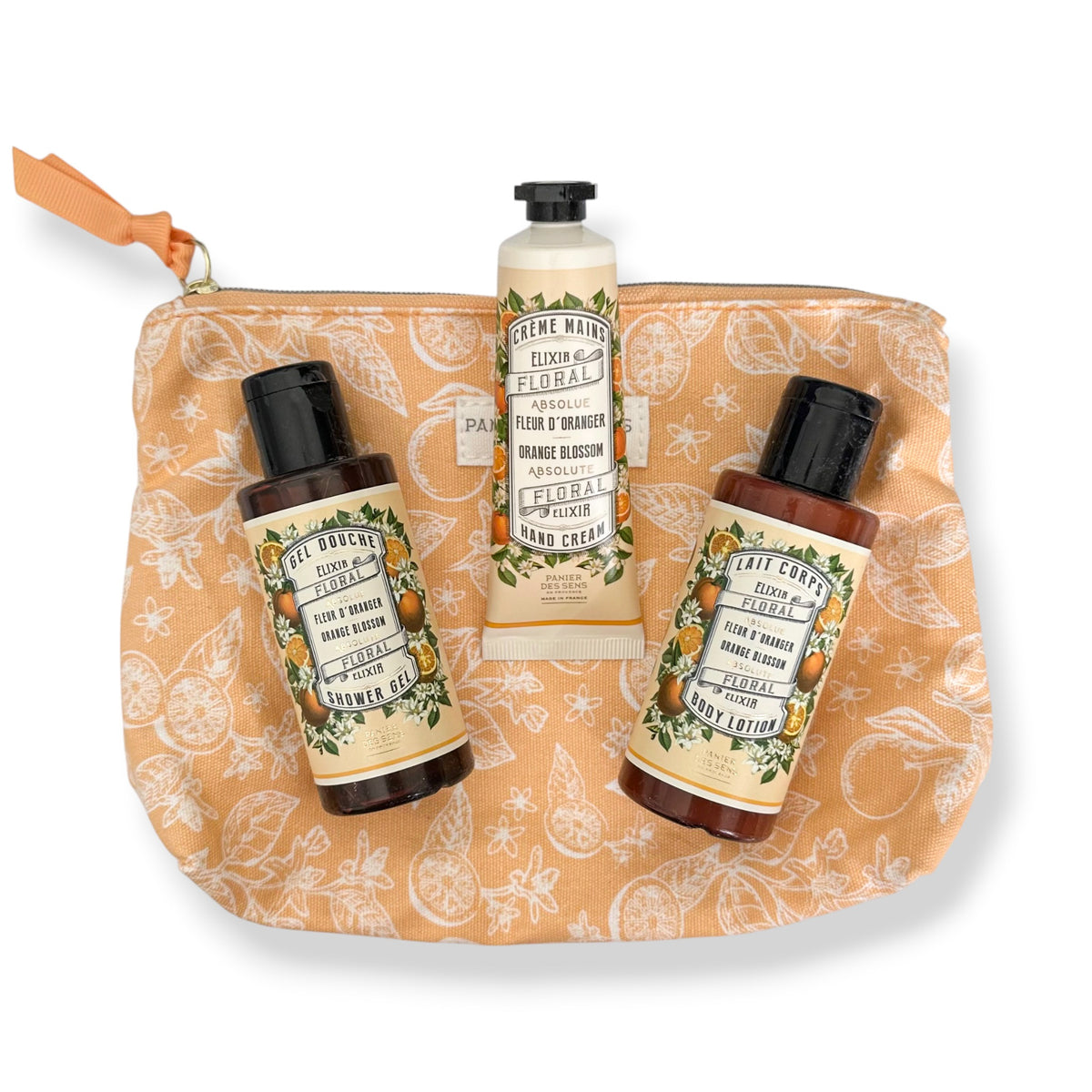 A gift set of bath and body products from Panier des Sens arranged on a peach zip pouch. The set includes a tube of Elixir de Clásico Hand Cream, a bottle of Citron Sabor Shower Gel, and a bottle of Citron Sabor Foot and Hand Wash, all with orange and green labels, set against a plain white background.
