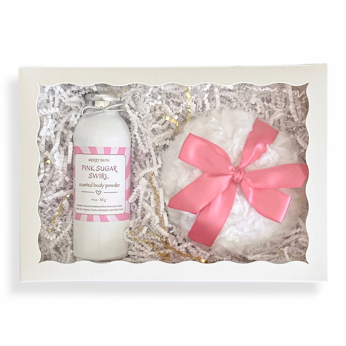 A gift set containing a bottle of 'Pink Sugar Swirl' natural body powder and a fluffy white bath bomb wrapped in a pink ribbon, presented in a white box filled with white shredded paper.
