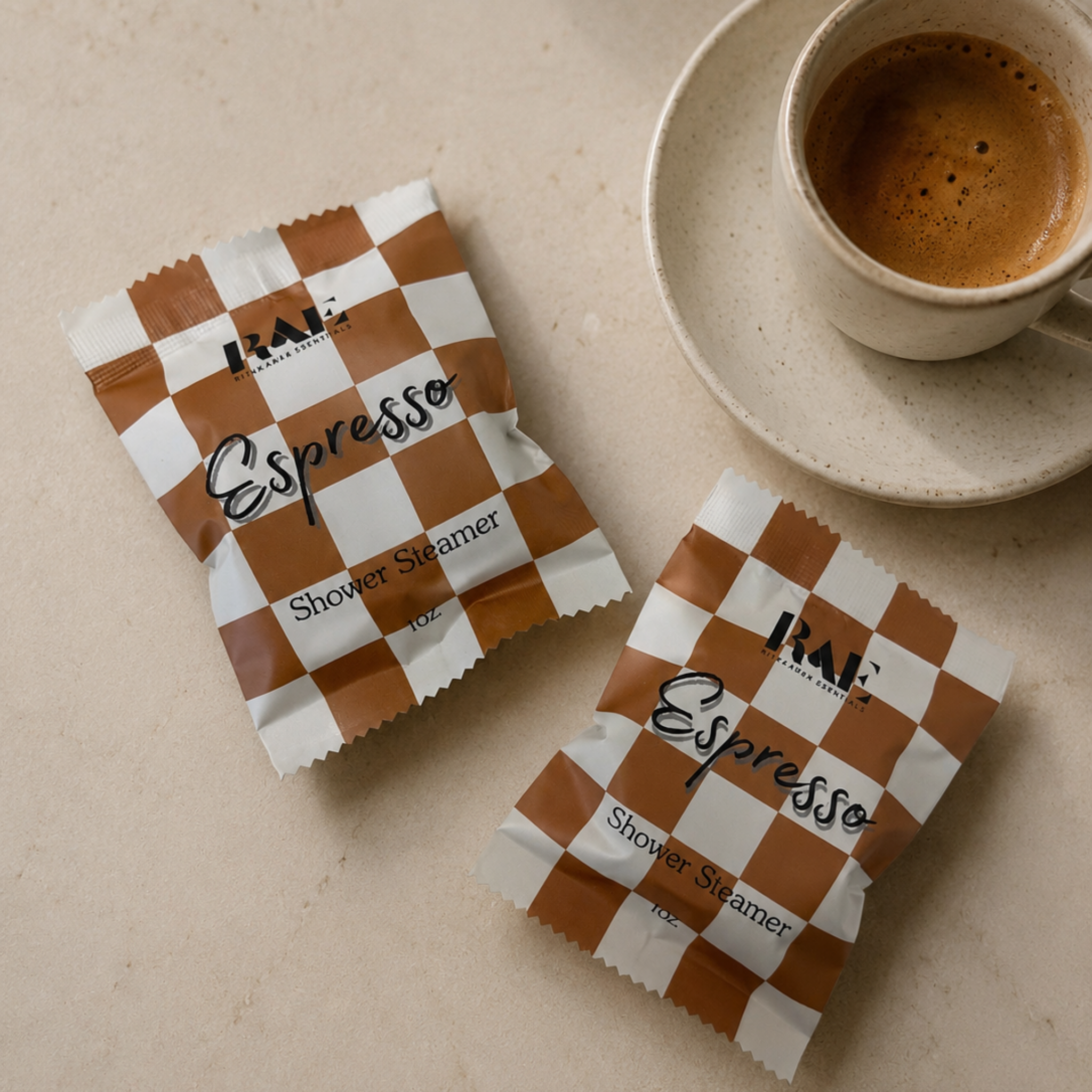 Two packets of 'Espresso' shower steamers on a beige surface with a cup of coffee.