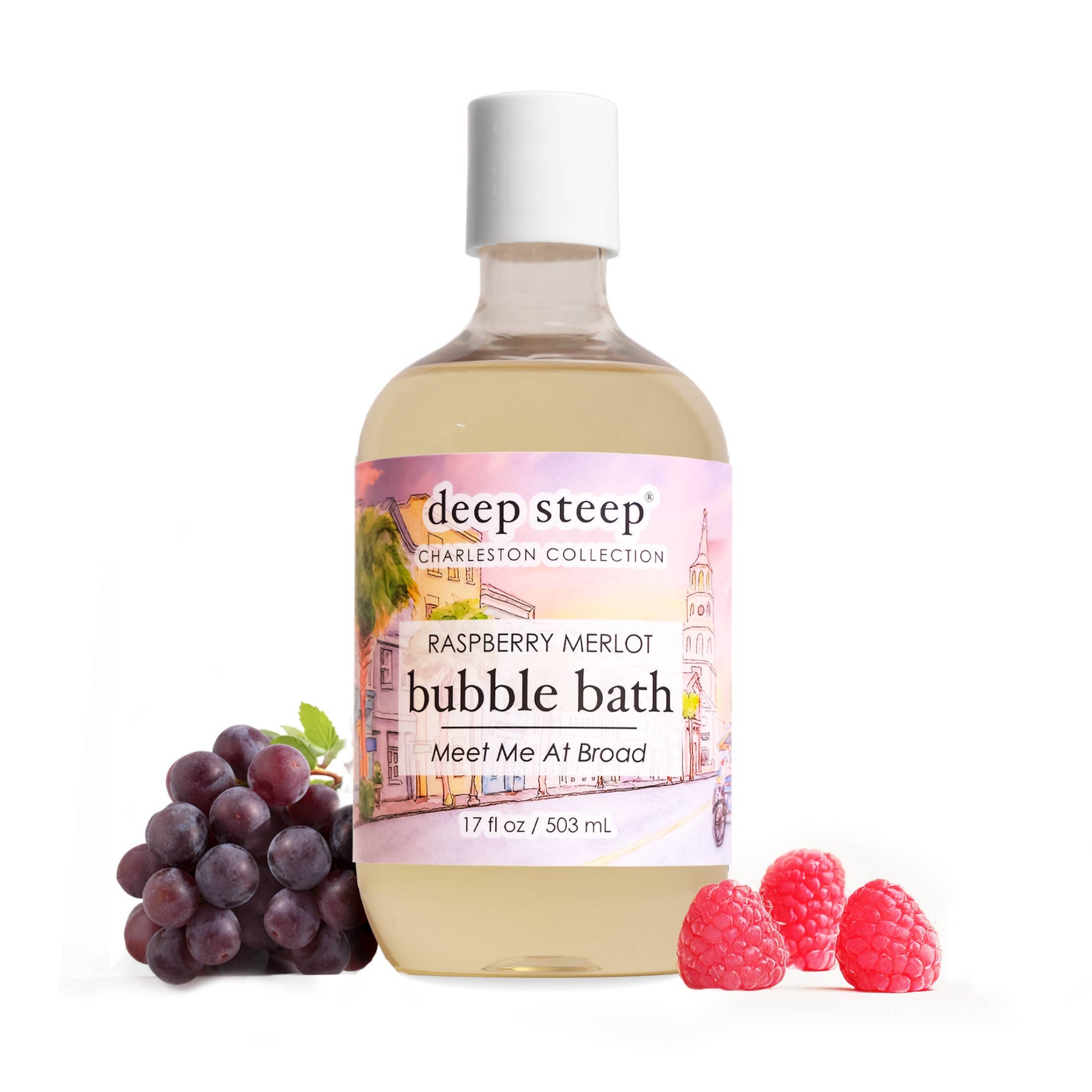 A bottle of deep steep Charleston Collection Raspberry Merlot bubble bath, styled with a cluster of dark purple grapes on the left and three fresh raspberries on the right, against a solid white background.