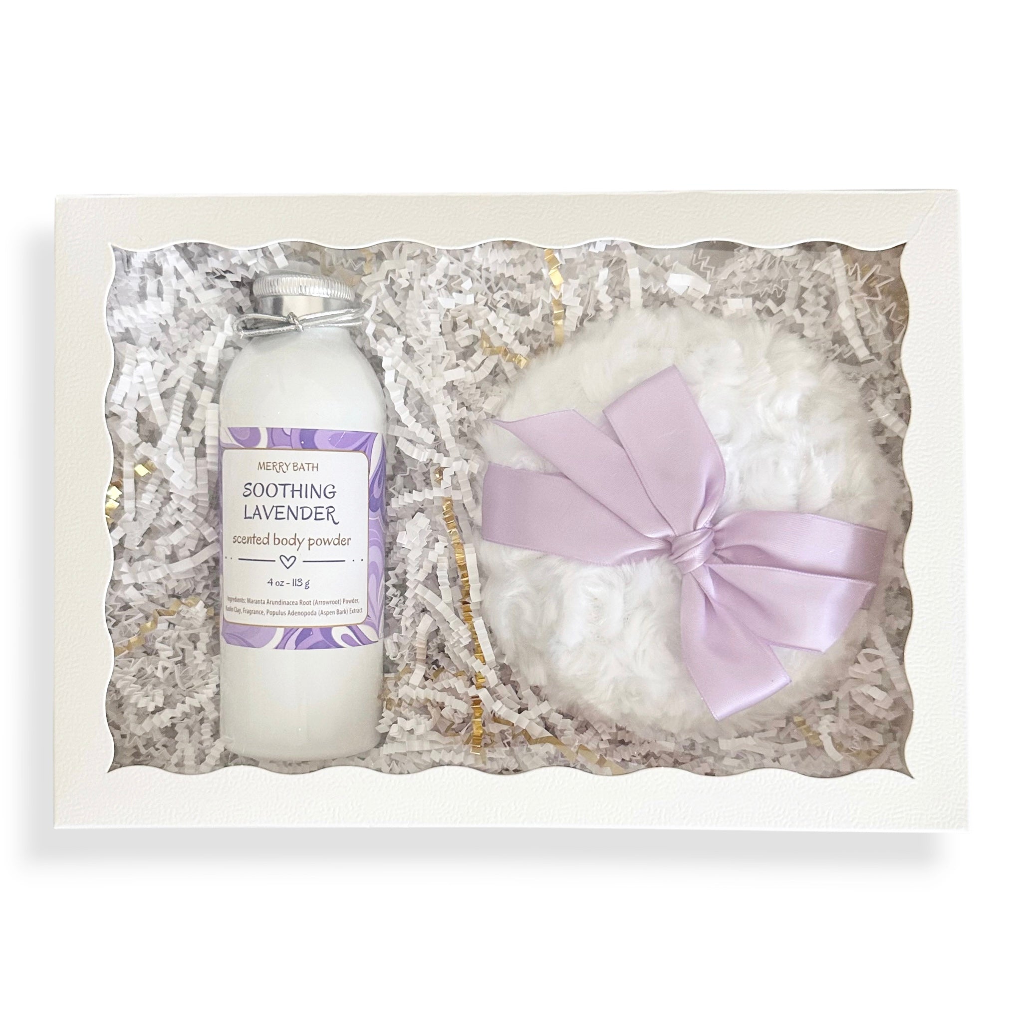 A gift set in a white box with shredded paper filler, containing a bottle of Mended Skin Soothing Lavender infused body powder and a white bath bomb with a light purple ribbon bow.
