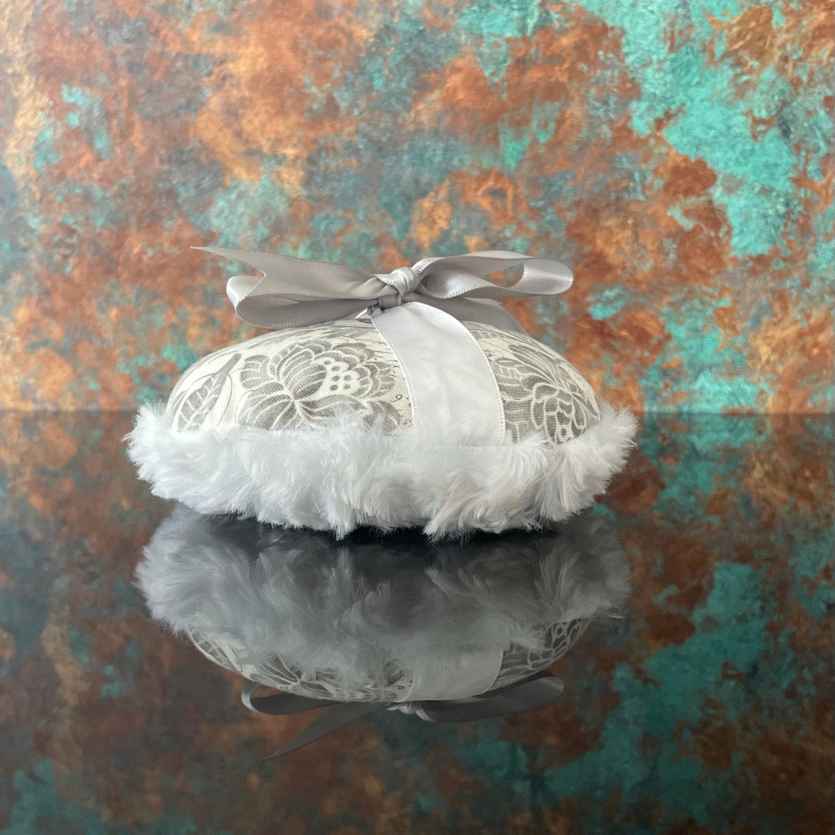 Large circular powder puff with gray floral top, white fluffy trim, and pale satin bow