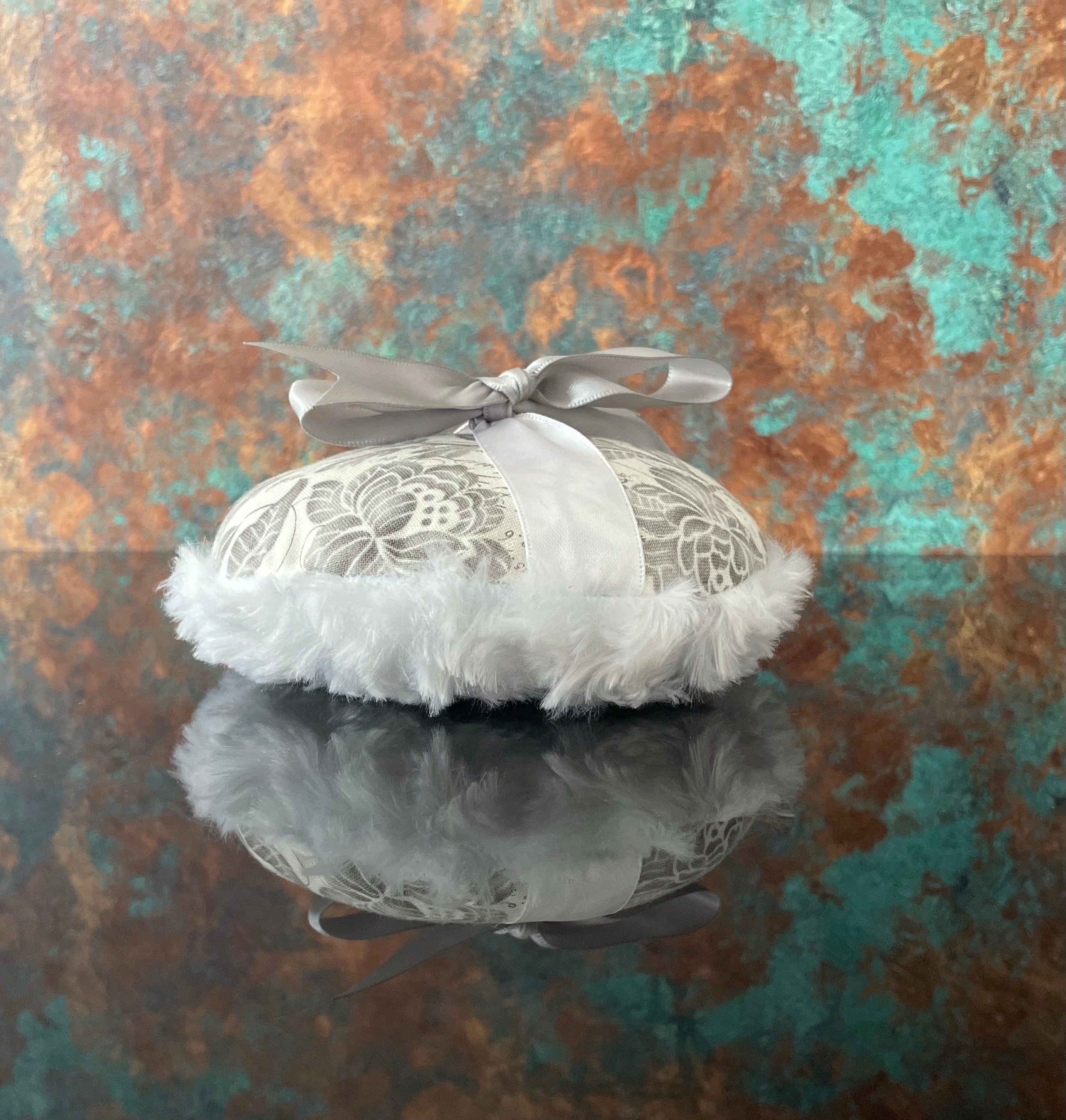 Large circular powder puff with gray floral top, white fluffy trim, and pale satin bow
