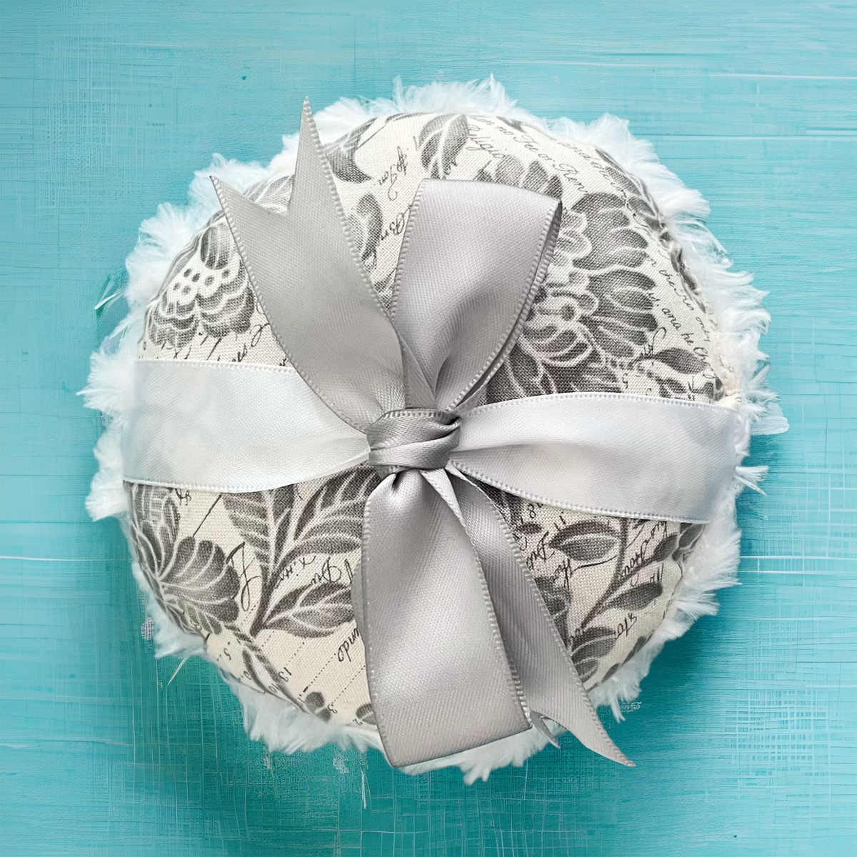 Floral gray-and-white powder puff with wide satin bow and fringed white lace edge